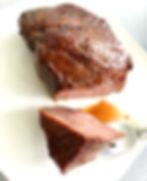 A grilled steak cut sits on a white plate, with a piece cut and ready to eat on a silver fork. Brown juices run onto white plate from the prepared meat.