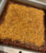 A silver baking pan holds a darker brown sticky looking dessert topped with lighter brown chopped nuts.