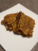Two brown, square dessert bars lay stacked on a white plate.