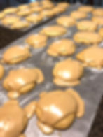 Rows of brown cookies with light tan icing sit in rows on white wax paper.