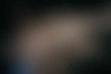 fotografia artistica em estúdio, com fundo escuro. mulher tatuada dança com 2 leques par fan veu. tem o corpo coberto pelo veu e a transparencia deixa ver sua silhueta