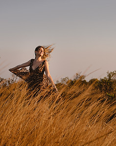 Foto de um ensaio externo mostrando uma mulher dançando com cabelos ao vento em meio ao capim em tons dourados da Serra do Rola Moça.