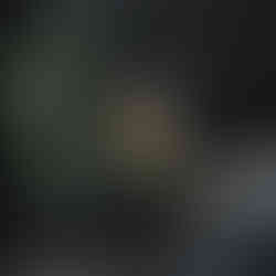 Woman in yellow hat and coat sitting on a pink and blue bench with tropical leaves and a pink background.