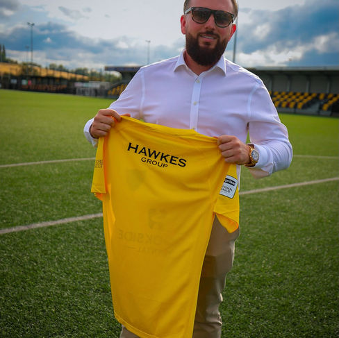 Hawkes Group Managing Director unveiling the new Harborough Town FC shirts, celebrating the company's support for local football alongside its demolition, earthworks and plant hire services.