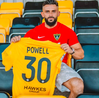 Harborough Town FC player Callum Powell holding the club's official shirt featuring Hawkes Group, specialists in demolition, earthworks and plant hire, as the team's shirt sponsor.