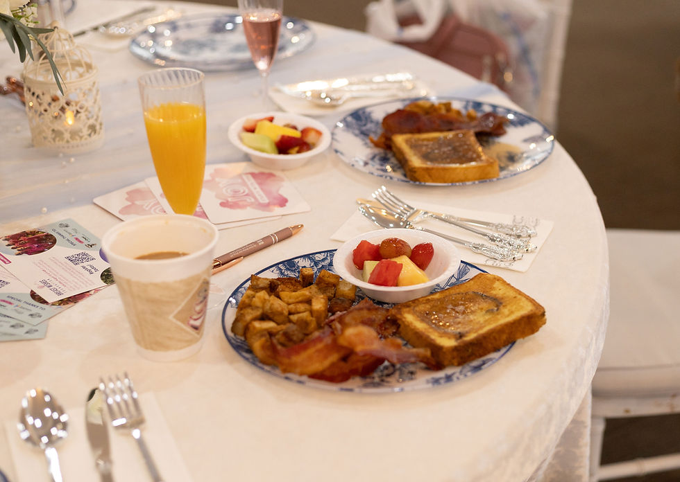 Plates of French toast, fruit, and bacon with orange juice.