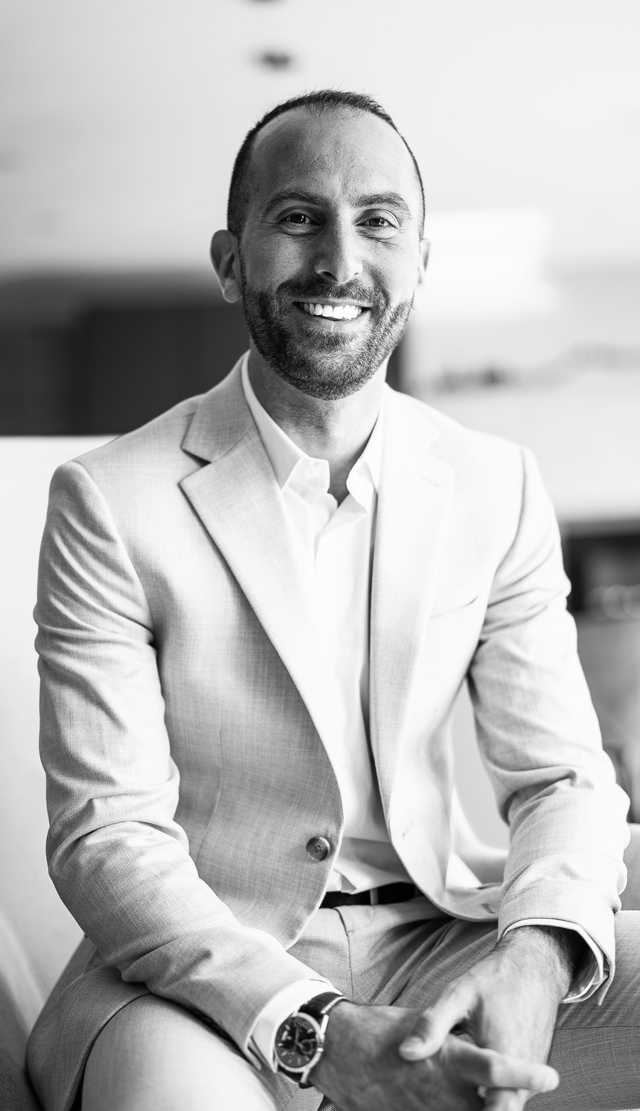 Charbel Daniel smiling, seated, in a light blazer, black and white portrait