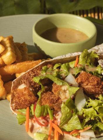 Wrap with lettuce, fried chicken and fries on a plate with sauce close up