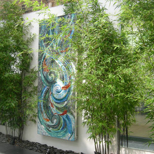 A wall mounted fish and water mosaic flanked by bamboo plants 