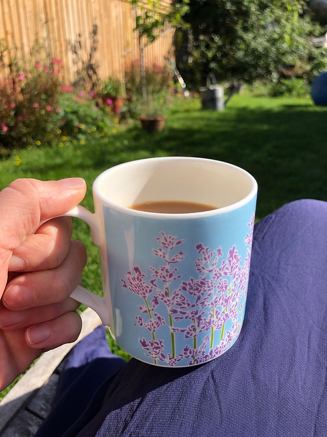 tea in a blue mug with a purple lavender flower design being held by a hand in the garden 