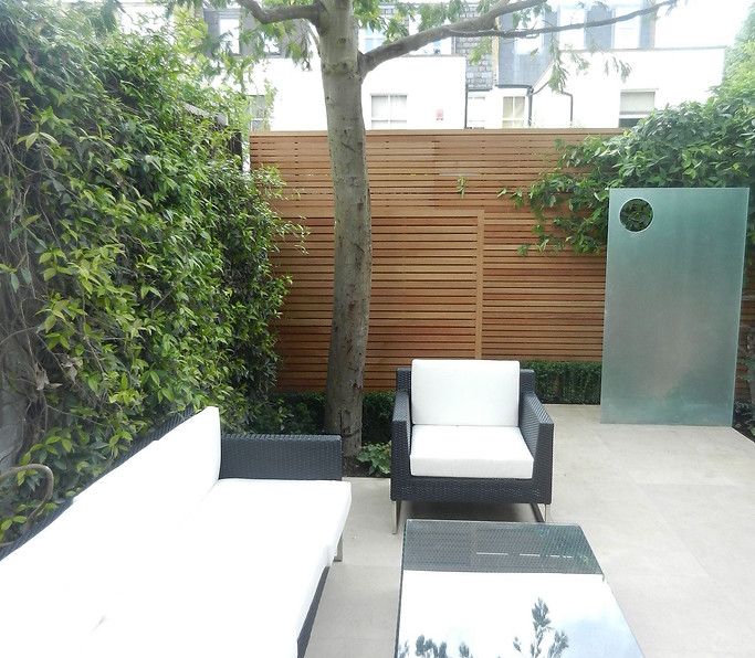 A contemporary garden with smart outdoor furniture, a glass sculptural feature and horizontal
slatted hardwood trellis.