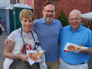 Smiling man and two older adults holding pizza slices outdoors.