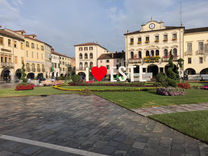 Sunny Este town square with large 'I ❤️ ESTE' sign, historic buildings.