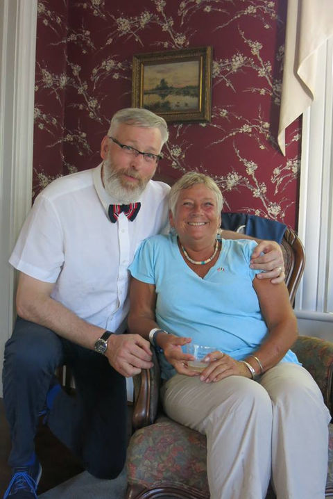 Smiling man with bow tie and woman with blue shirt indoors.