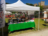 Outdoor vendor booth with TAPALCA flag, FedericoBerg banner, and castle background.