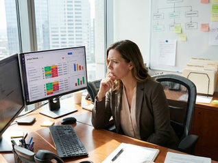 A professional female property manager sitting at her modern office desk, looking at a computer screen showing Monday.com dashboards
