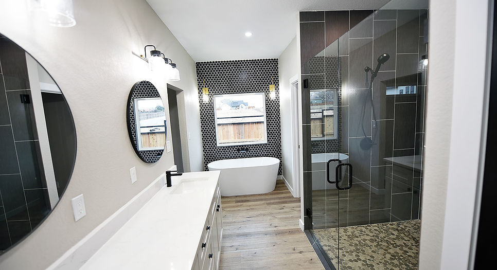 Contemporary master bath with generous shower pebble floor black vertical large format wall tile and freestanding tub with black cross pattern decorative tile and brass wall sconces