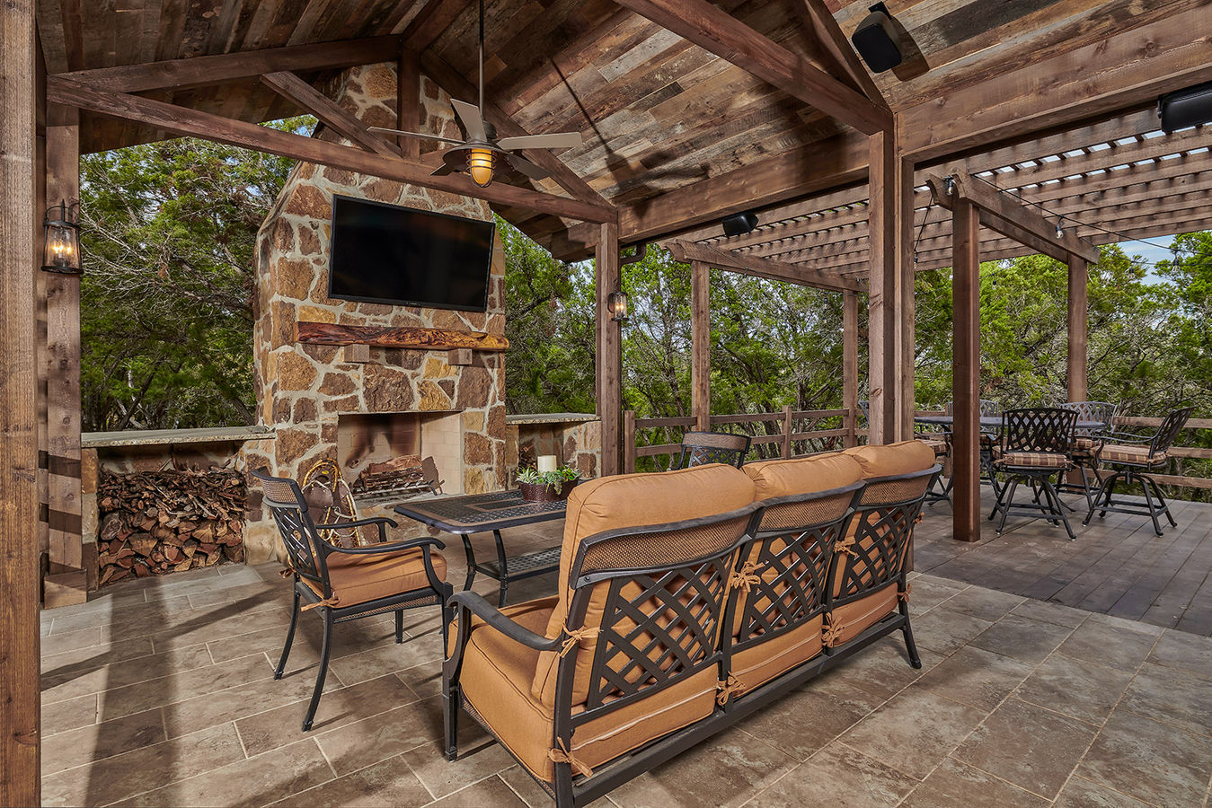 Covered seating area with stone wood-burning fireplace adjacent to trellised deck.