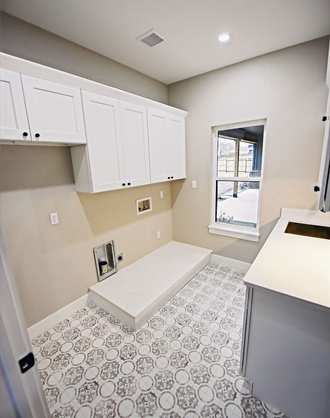 Faded decorative floor tile quartz plinth for washer and dryer refrigerator space white cabinetry with black hardware bathed in natural light