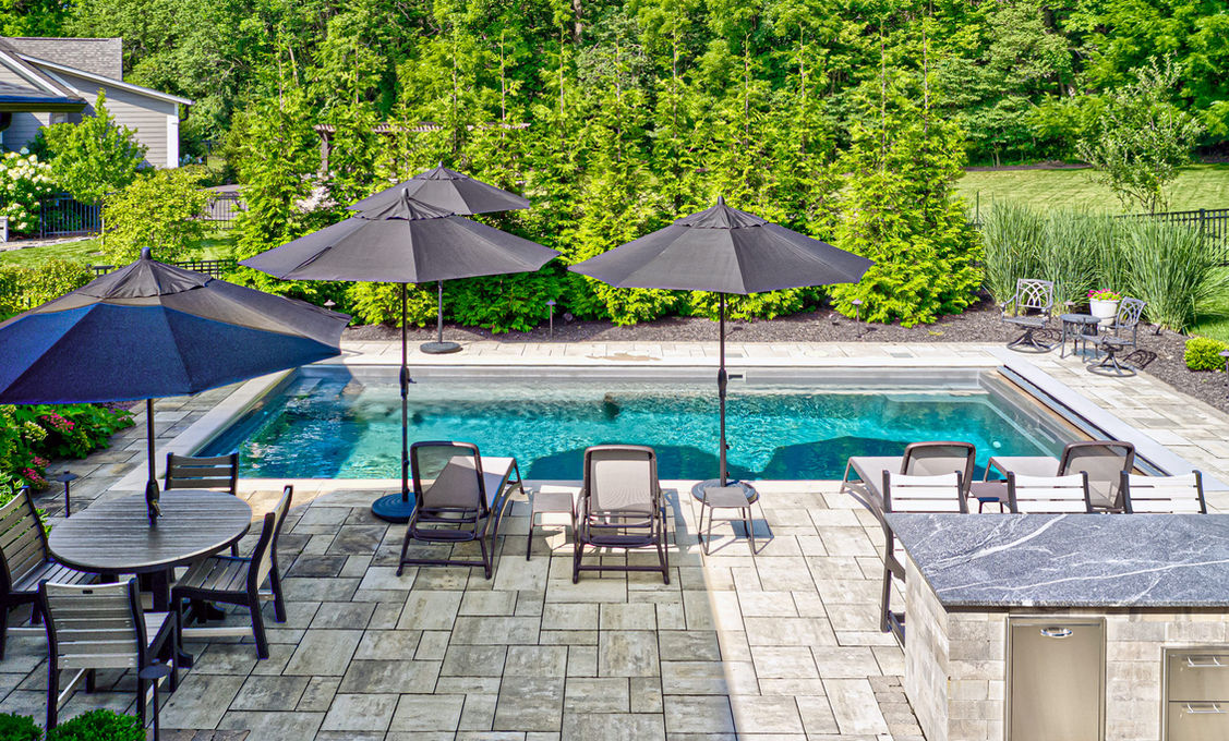 Backyard pool patio with lounge chairs, umbrellas, and paver hardscape.