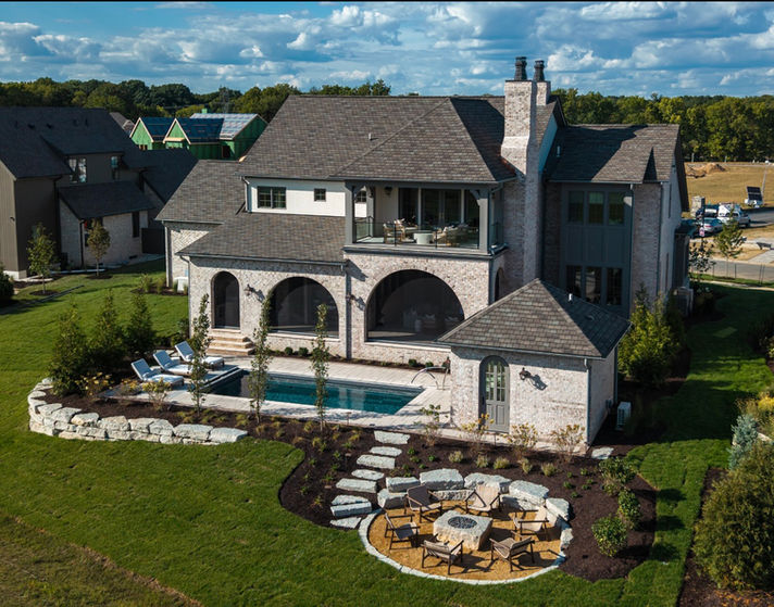 Pool and circular seating area around square firepit outside of large stone home