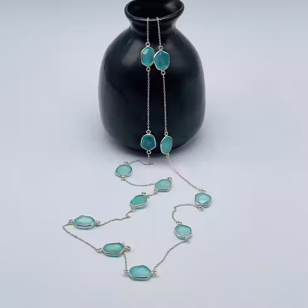 Silver chain necklace with aqua calci gemstones displayed on a black vase.