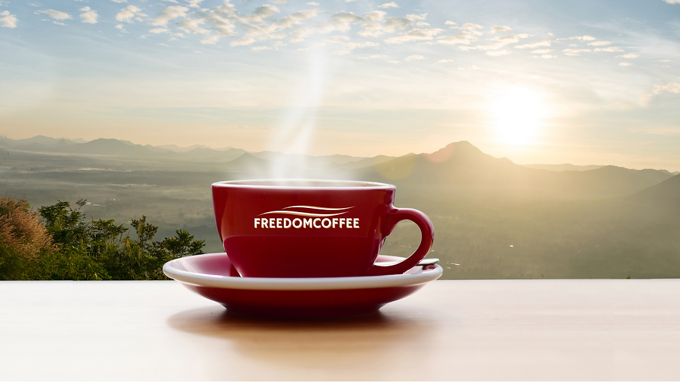 Tasse de café rouge estampillée "FREEDOMCOFFEE" fumante posée sur une table, avec vue panoramique sur les montagnes au lever du soleil.