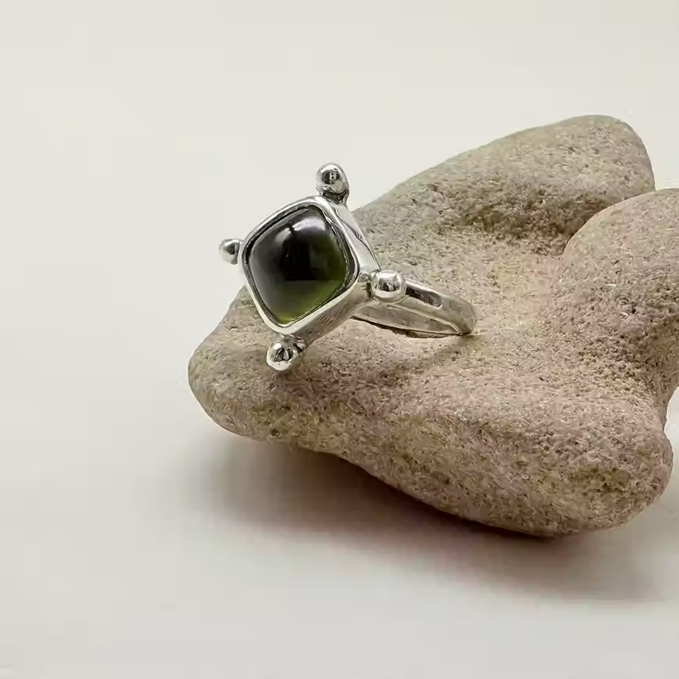 Sterling silver Peridot Compass Ring with square green gemstone and silver bead details on natural stone.