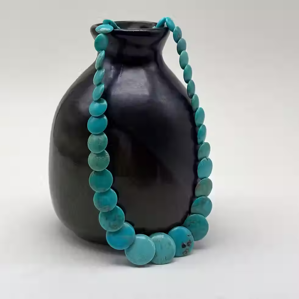 A turquoise necklace with smooth, round beads, displayed against a black ceramic vase.