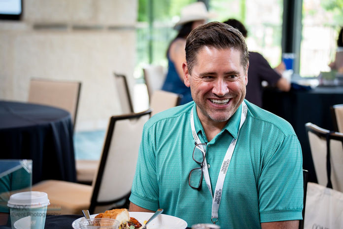 Smiling man in a teal polo shirt at a conference lunch.