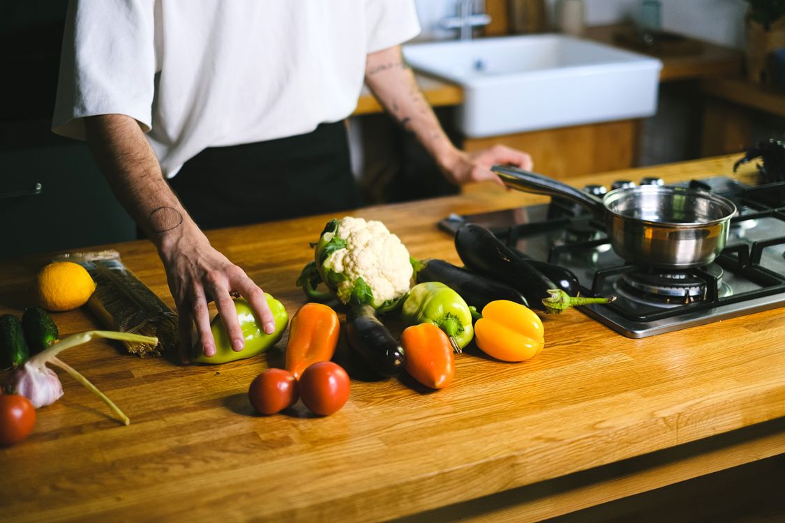 A cook arranging fresh vegetables on a wooden kitchen counter