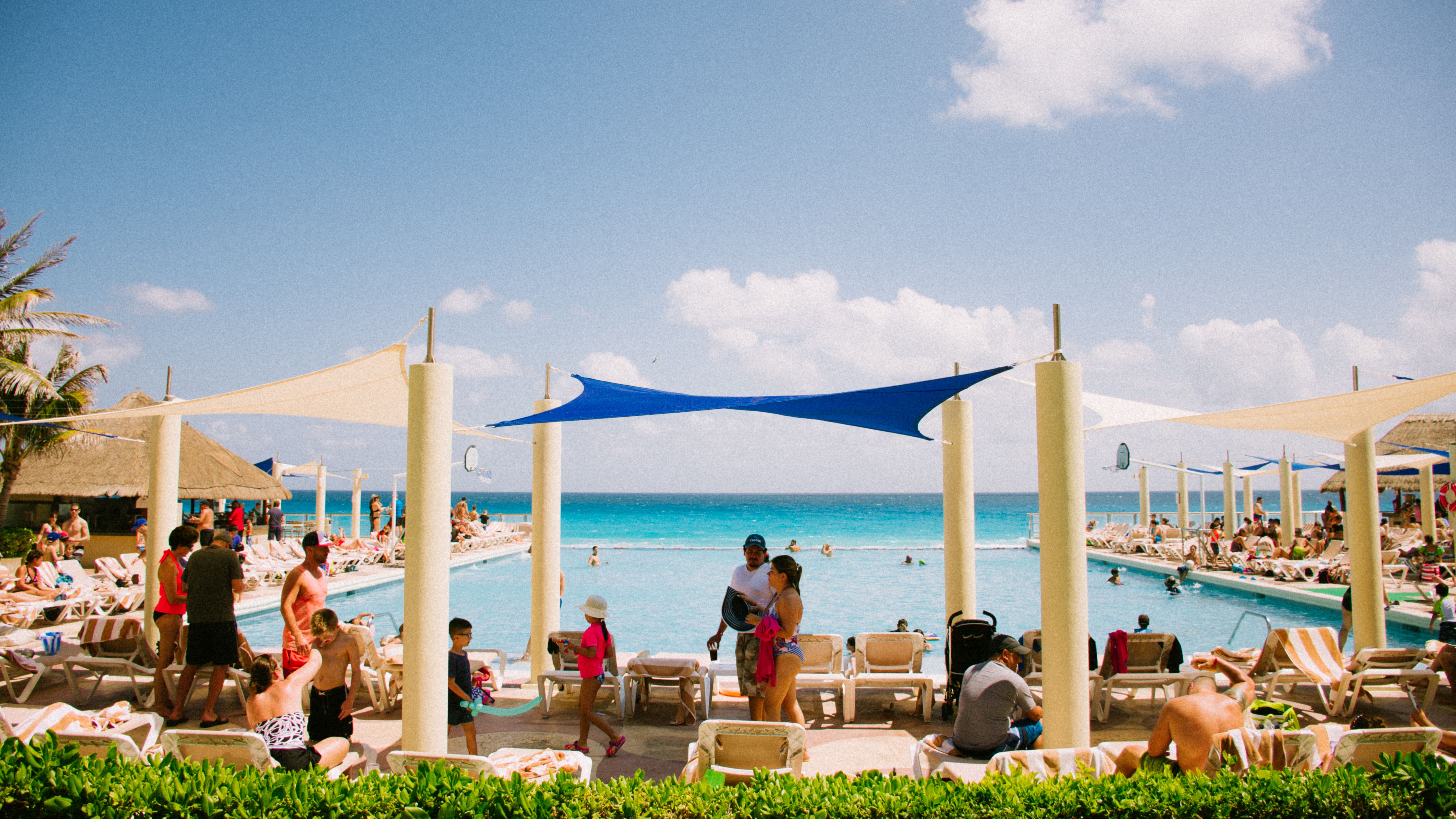Families relaxing beside a beachfront resort pool on a sunny day