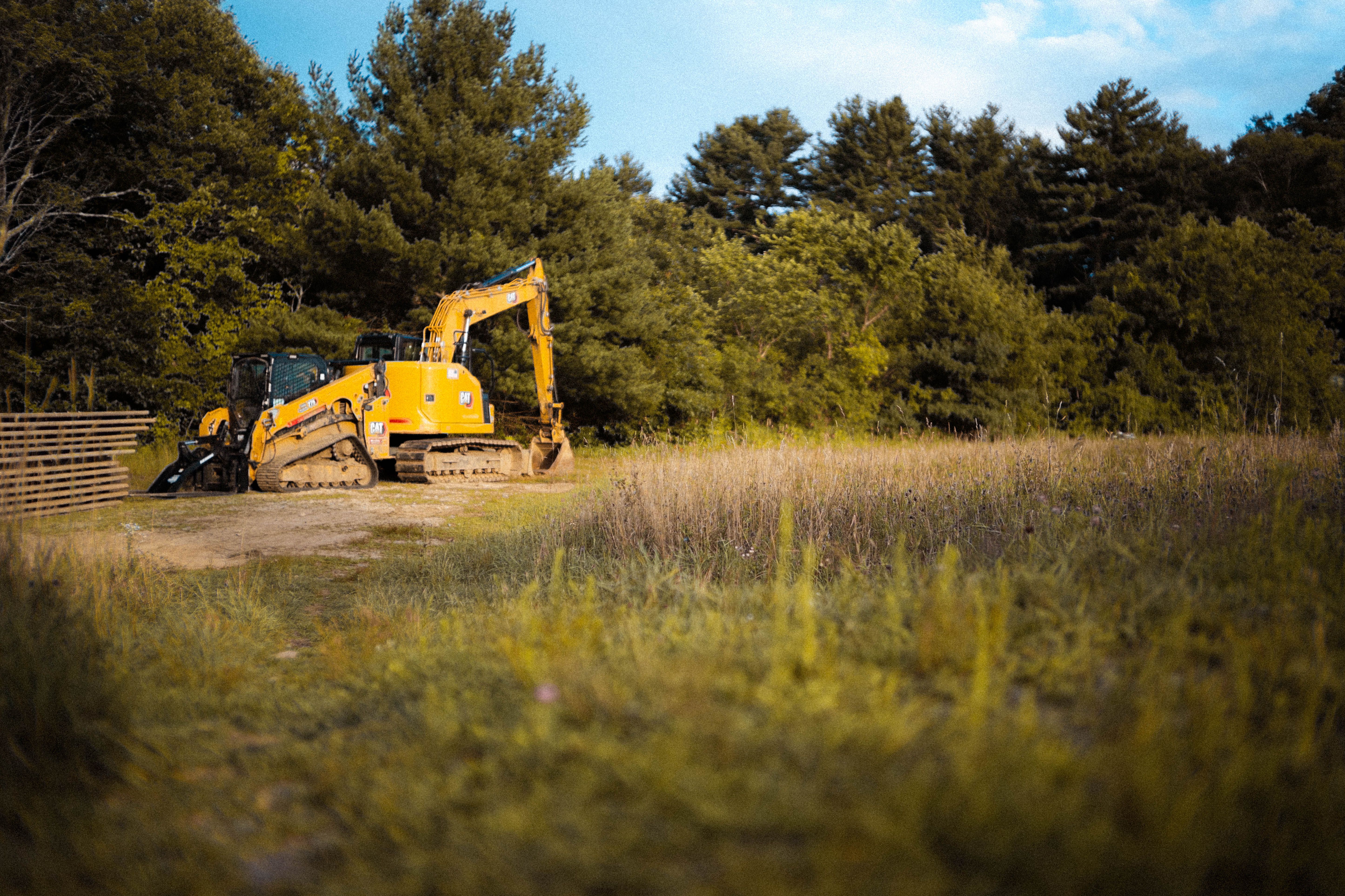 Yellow land clearing equipment working beside a wooded area