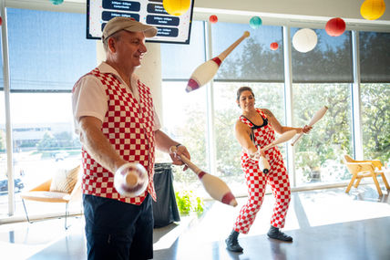 Two people juggling clubs in matching outfits indoors, ATX Event Photography.