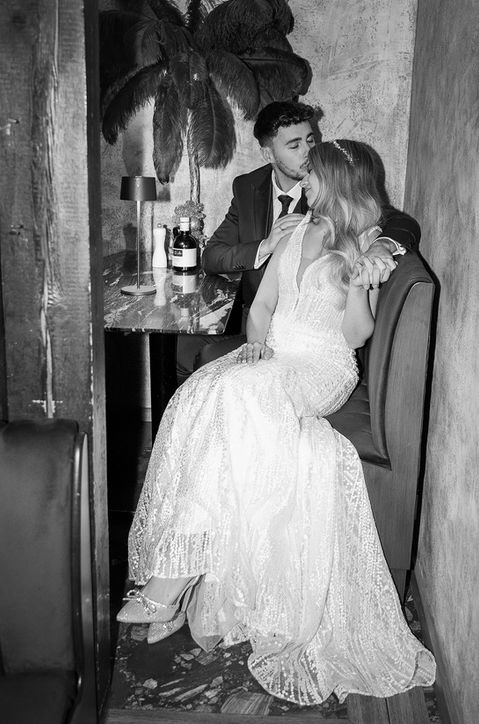 Intime Schwarzweißaufnahme eines Brautpaars, das zusammengekuschelt an einem Tisch sitzt. Nicole hat extrem faire Preise und wird von ihren Kunden als herzlich, empathisch und sehr professionell beschrieben.