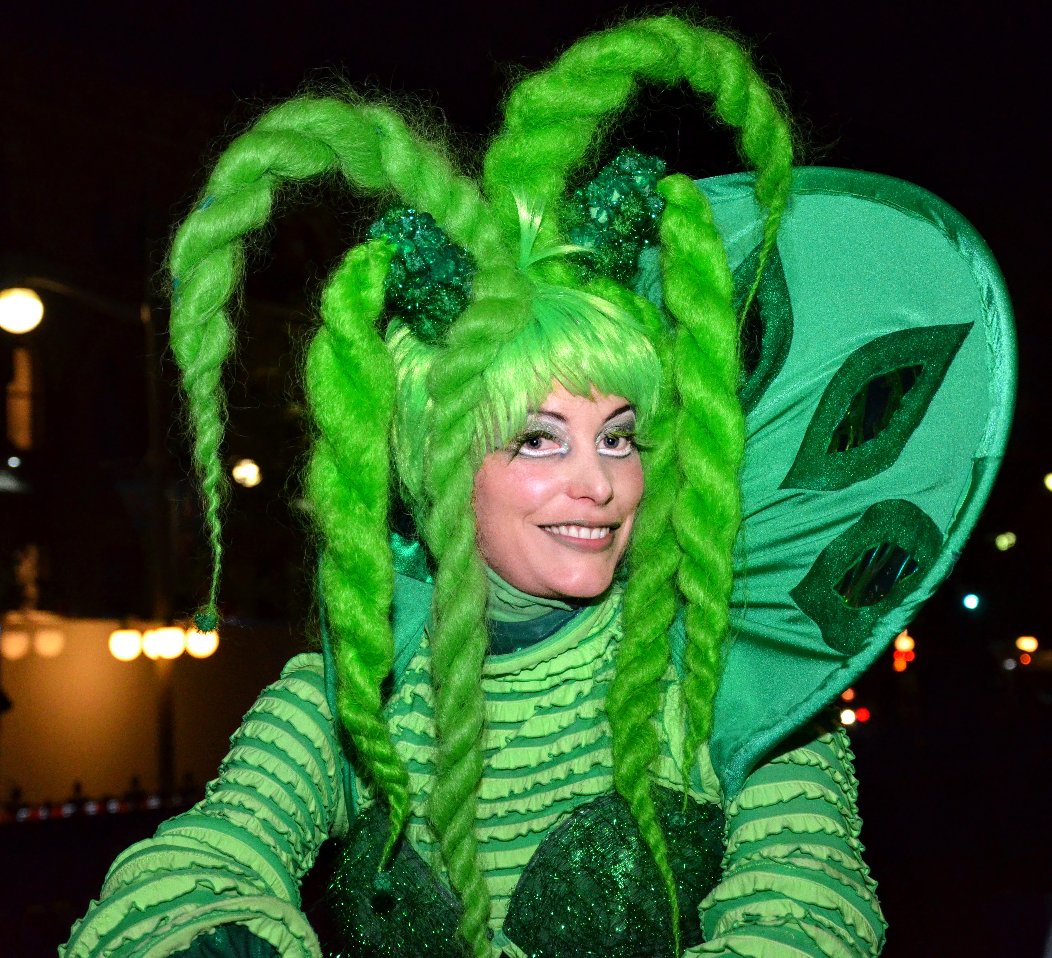 Émeraldine, artiste sur échasses énergique, habillée en vert scintillant, créant une ambiance vivante lors d'une fête d'entreprise.