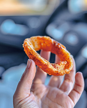 A hand holding a single onion ring in the car.