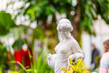 A stone statue in the middle of the fountain with trees in the background, at the conservatories in south bend.