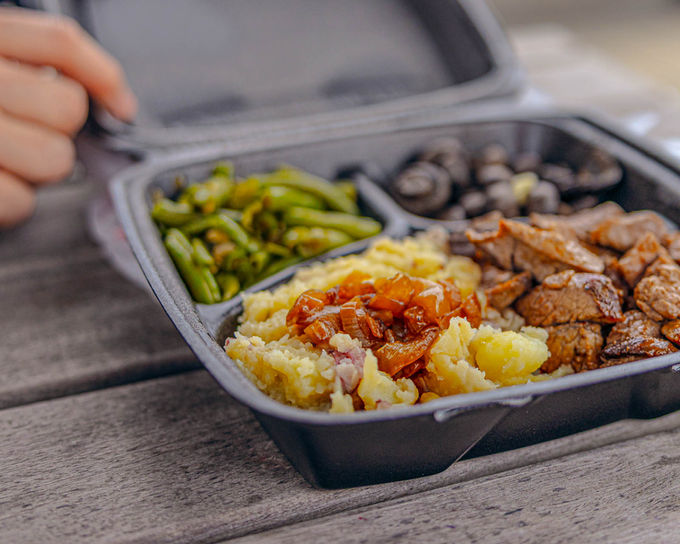 Large steak dinner in a black takeout container on a picnic table, from Neddermans steak house