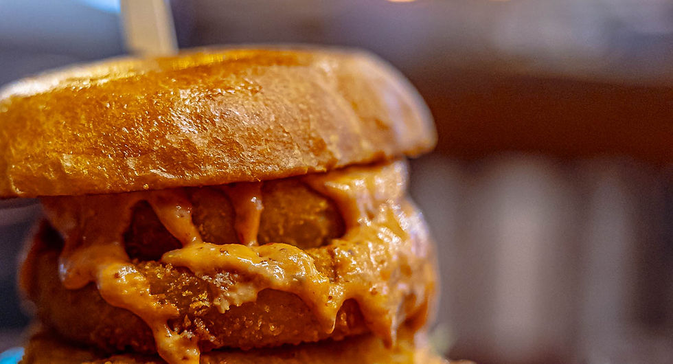 A large messy burger with onion rings and sauce on a plate.