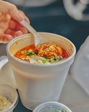 A personal scooping soup out of a takeout container in a car.