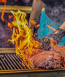 Woman flipping chunks of beef over a flaming grill.