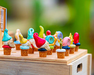 Small colorful ceramic sculptures displayed on cork stoppers at a pottery vendor table.
