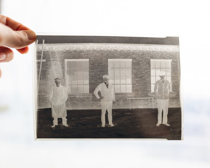 Film negative showing three factory workers posed in front of a brick factory building in Elkhart, Indiana.