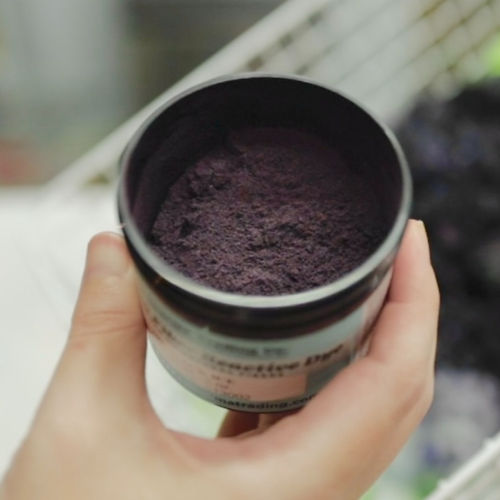 A hand holding a jar of fiber reactive dye in the color, black ice