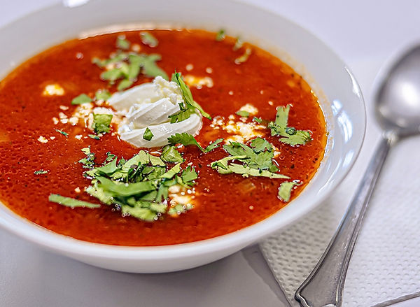Mexican ABC soup with sour cream, cheese and cilantro served at Waka Dog cafe. In a white bowl, with a spoon an napkin to the right.