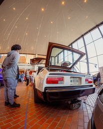 White classic car rear with open door and people gathered nearby at Century Center South Bend Auto Show