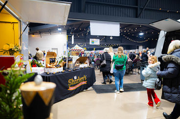 Crowds walking through the Mistletoe Market inside the Elkhart County Community Center at the Elkhart County 4-H Fairgrounds, with vendor booths and holiday lighting.