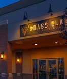Front entrance of Brass Elk Brewing in Elkhart, Indiana, with glowing sign and brick columns at dusk.