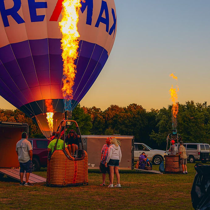 Hot air balloons launching at sunset during the Marshall County Blueberry Festival, with crews igniting burners and attendees watching from the field